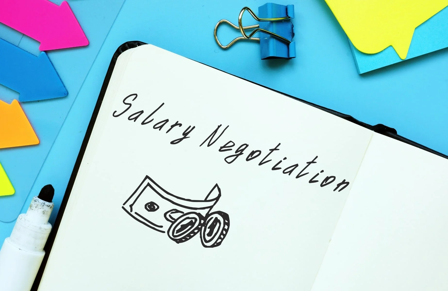 A notebook page with the handwritten words 'Salary Negotiation' accompanied by a doodle of currency notes and coins, surrounded by colorful arrow-shaped sticky notes and blue paper clips on a bright blue background. How to negotiate salary during interviews.
