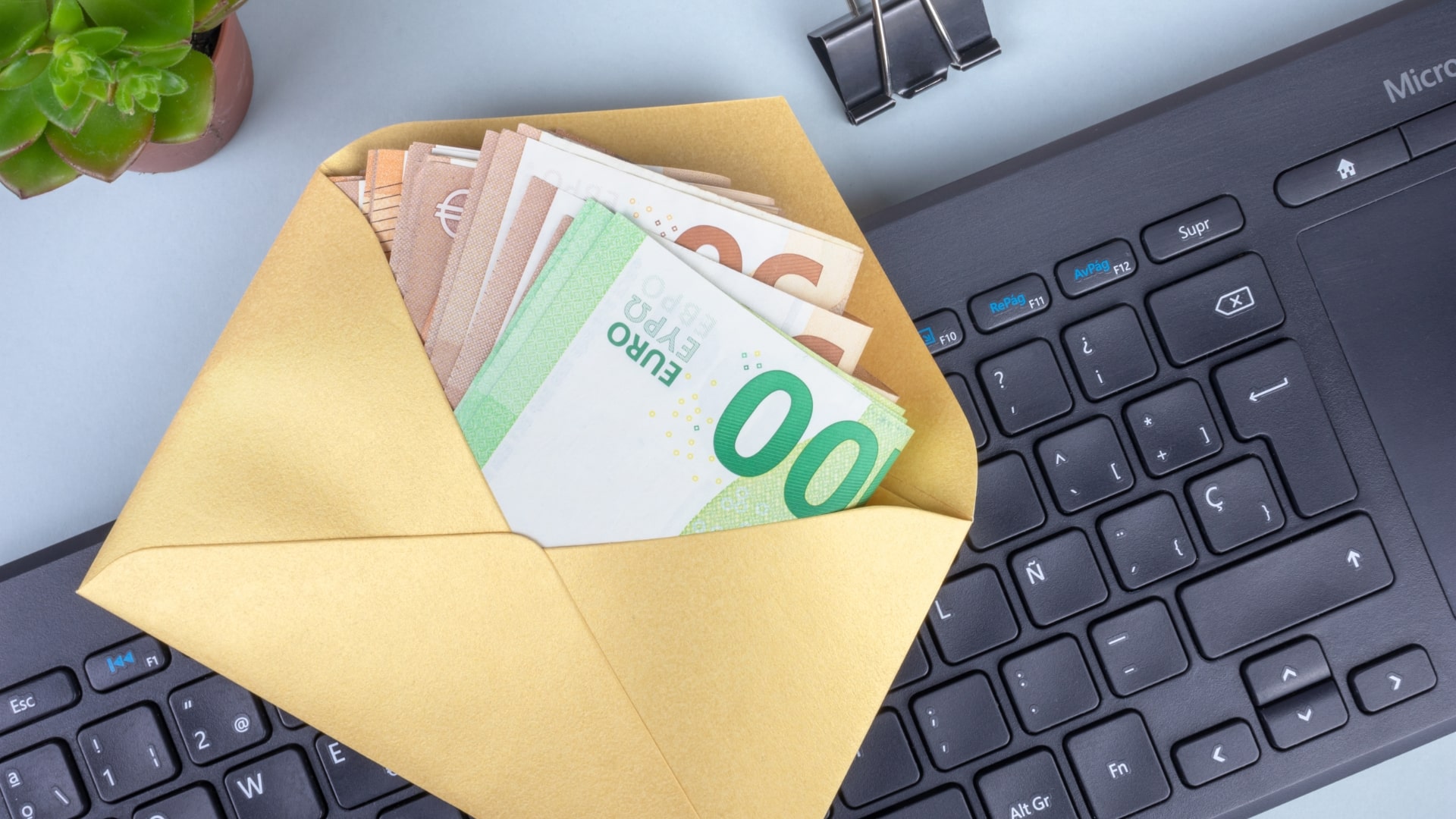 An envelope filled with euro banknotes placed on a keyboard, symbolizing the impact of the new salary law on workplace transparency and pay practices.