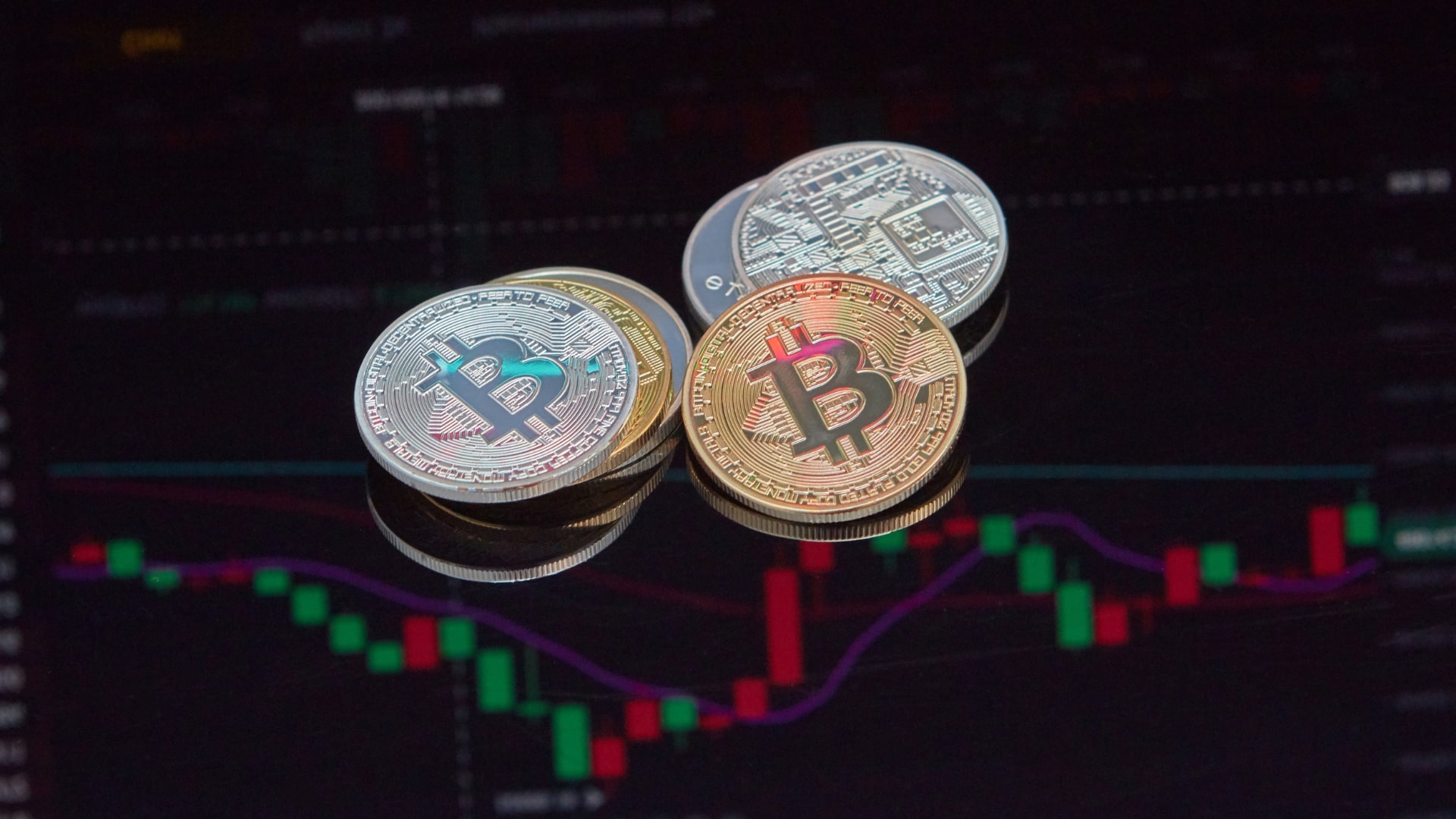 Physical Bitcoin coins stacked in front of a trading chart with red and green candlesticks, symbolizing the volatility of the crypto bear market.