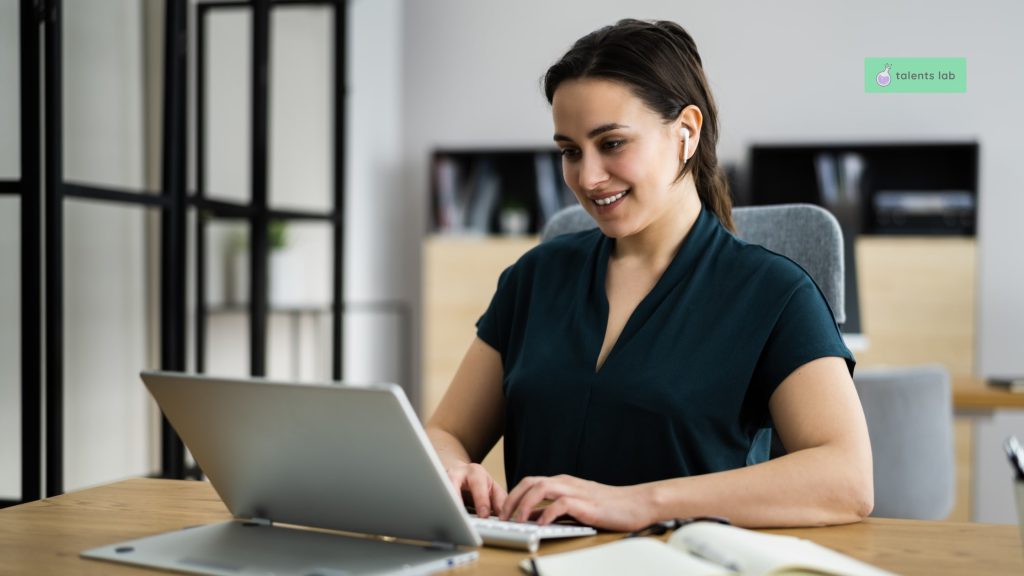 Smiling woman wearing earphones during a remote job interview, typing on a laptop, representing a positive and professional interview process.